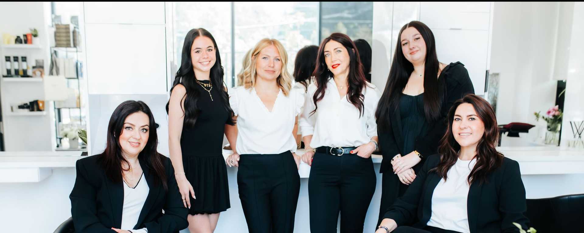 Group of six women in a salon setting, wearing stylish black and white outfits.